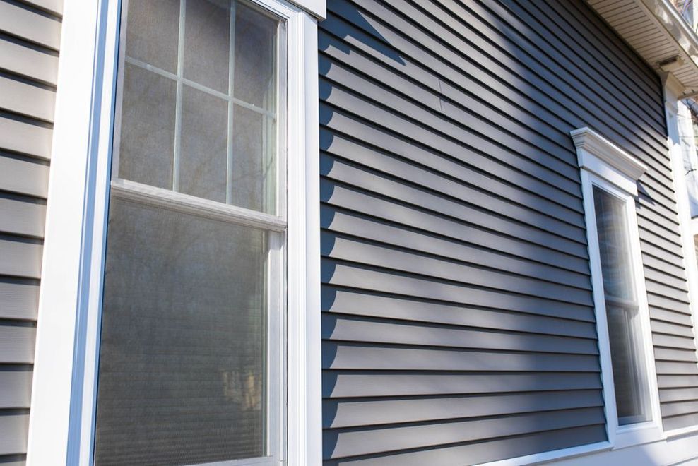 Side of a house with gray siding and two white-trimmed windows