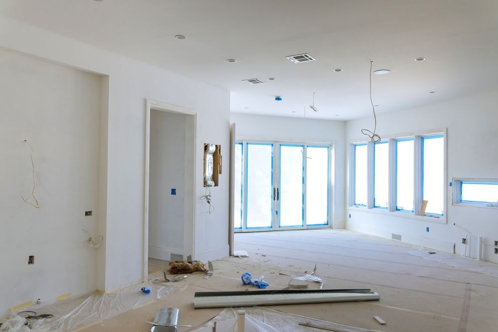 Bright unfinished living room with white walls, large windows, and construction debris on the floor