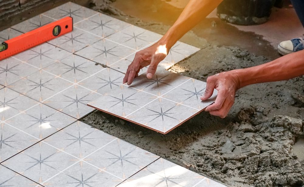 Hands laying patterned floor tiles beside a level on wet mortar
