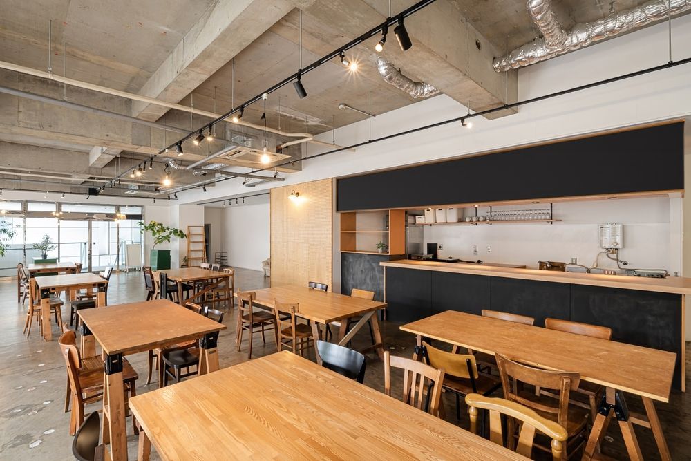 Bright, modern cafe with wooden tables, stools, and a black counter under exposed ceiling ducts