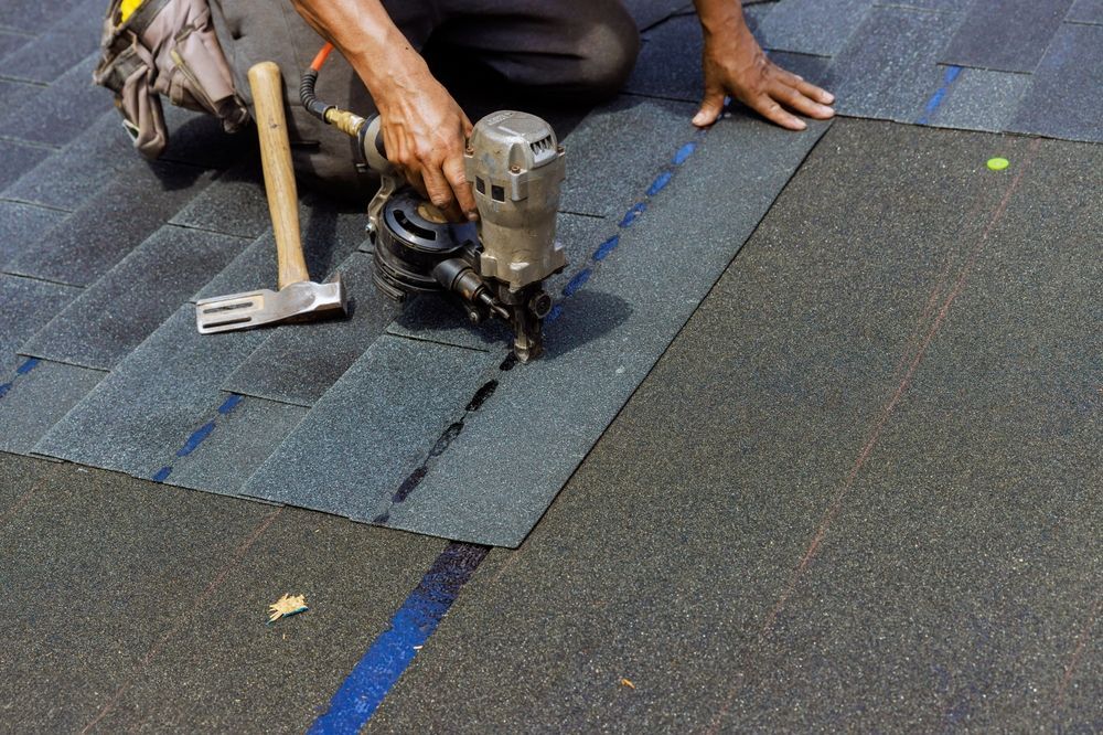 Worker repairing a roof with a nail gun beside a hammer on dark shingles
