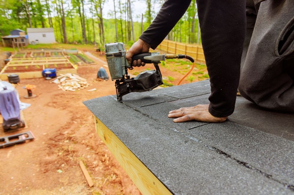 Worker using a nail gun to install roofing on a house under construction