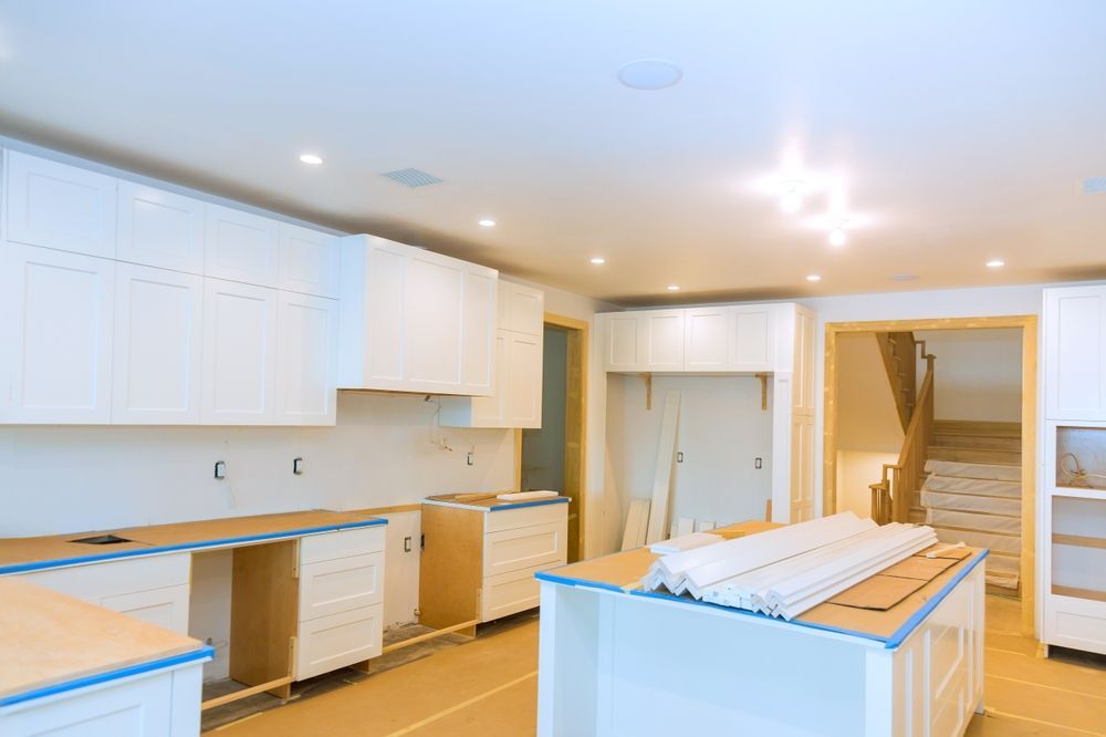 Bright unfinished kitchen with white cabinets, islands, and staircase in background