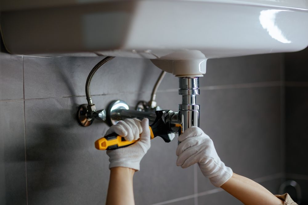 Hands tightening a bathroom sink drain pipe under a white sink with a wrench.