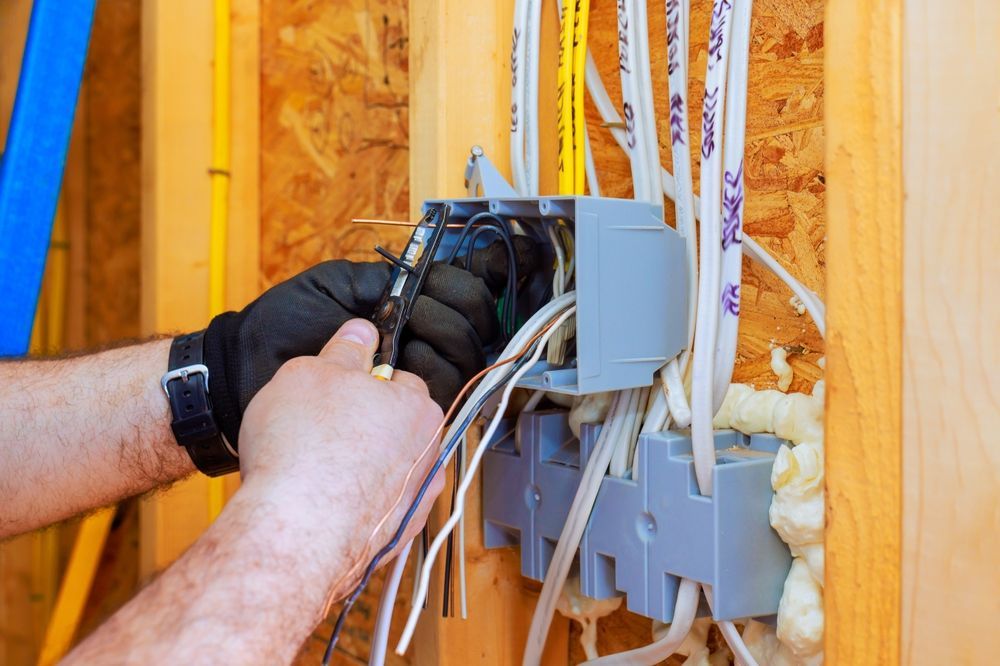 Electrician wiring a wall electrical box with multiple cables in a framed wall.