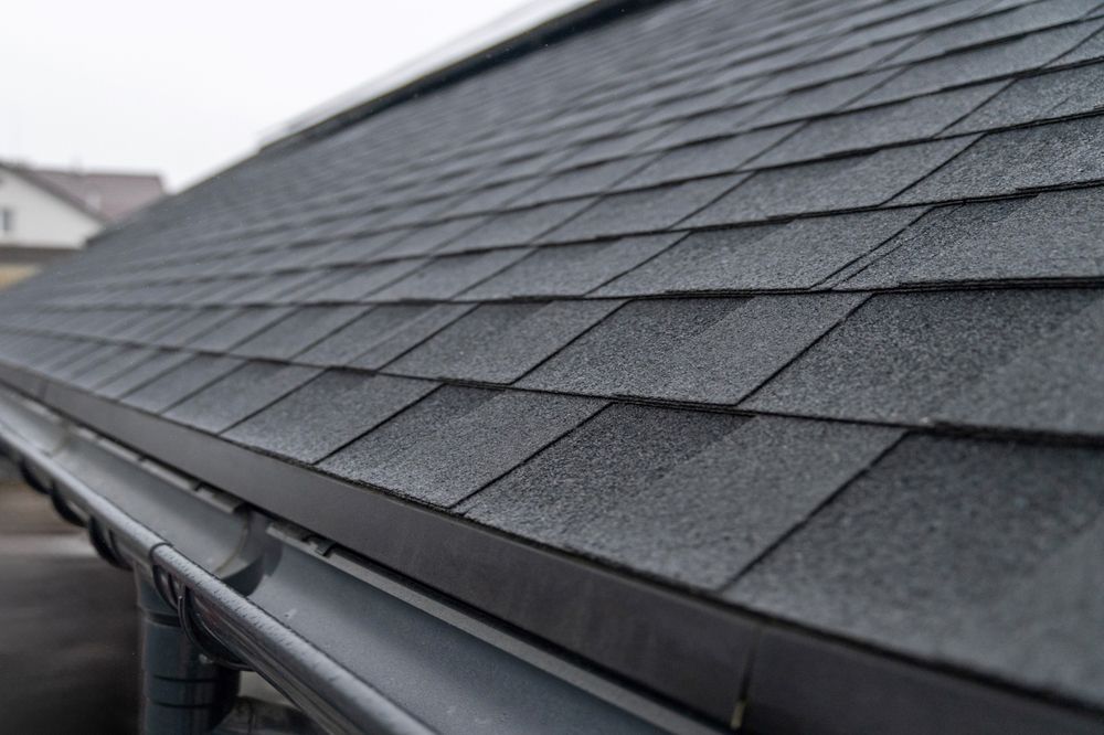 Close-up of a dark gray shingle roof and gutter on a sloped house