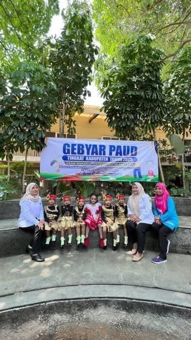 Children in costumes with adults, sitting beneath a banner that reads