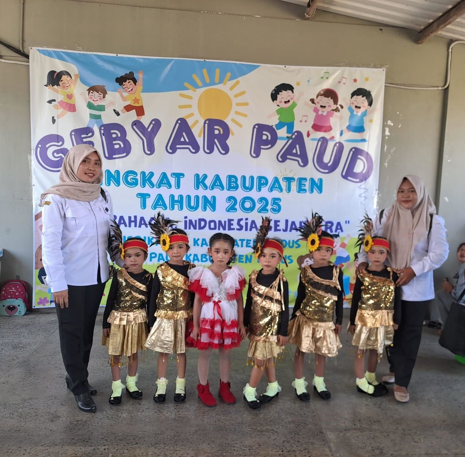 Group of children in costumes and teachers in front of a banner at an event.