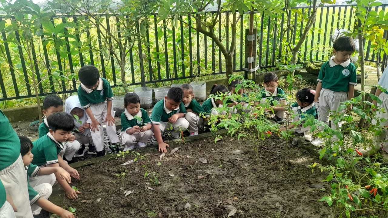 Children in green uniforms gardening together in an outdoor garden.