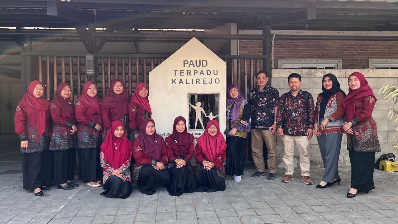 Group posing outside a building with a sign reading “Pundi Terdel KALIREJO,” some in red outfits and hijabs