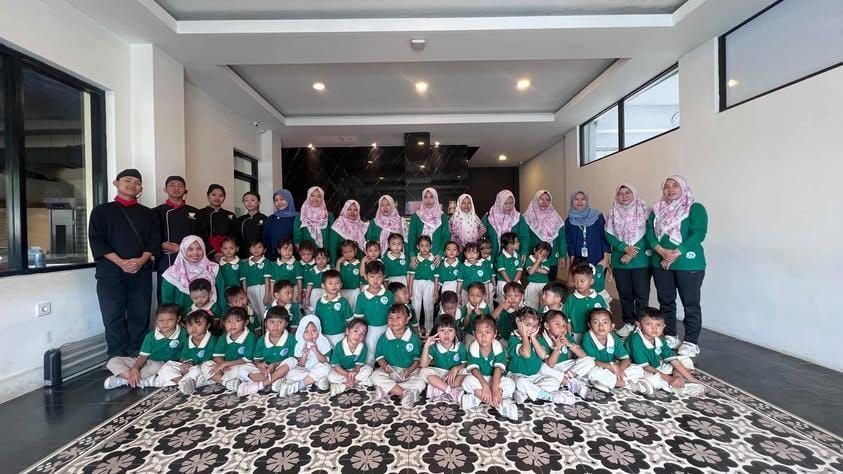 Group photo of children and teachers, all in green uniforms, posing indoors.