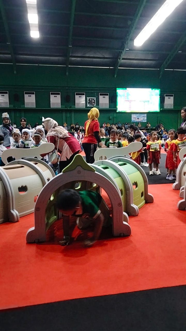 Child crawling through a play tunnel during an event. Other children and adults are in the background.
