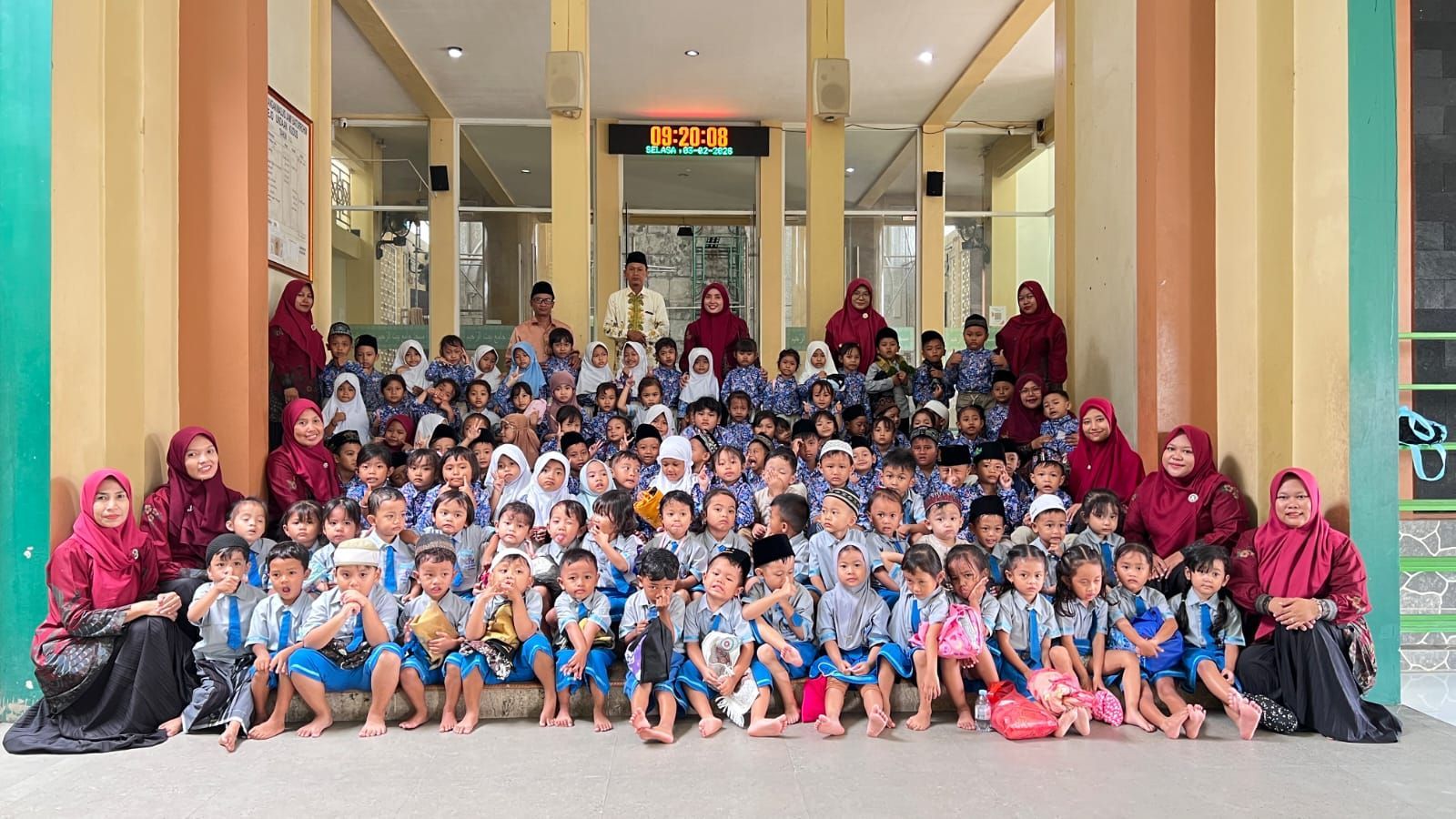 A large group of students and teachers in school uniforms and headscarves posing for a group photo in front of a building.