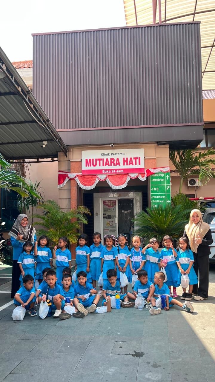 Group of children in blue uniforms posing outside Mutiara Hati building with two adults holding a banner