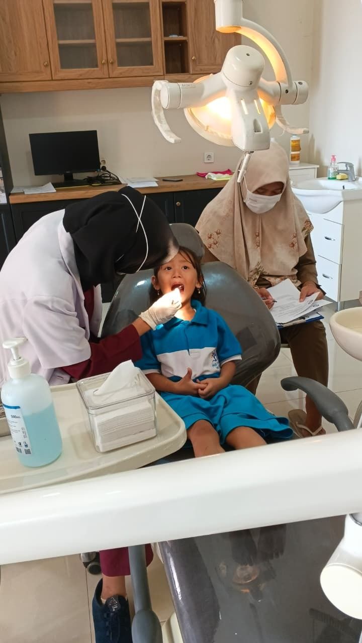 Child sitting in a dental chair while two masked clinicians examine their mouth in a dental office