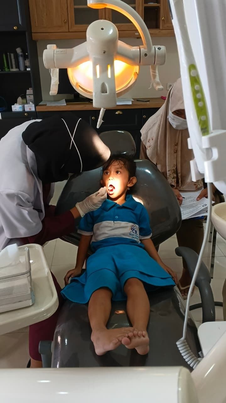 Child lying in a dental chair during an oral exam, with dentist and overhead exam light nearby