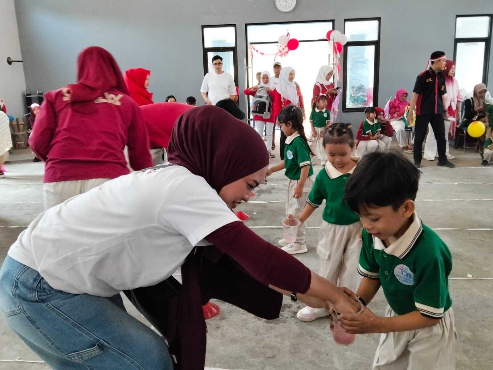 Adults and children in a bright room playing a hand game, with two boys in green shirts in front.