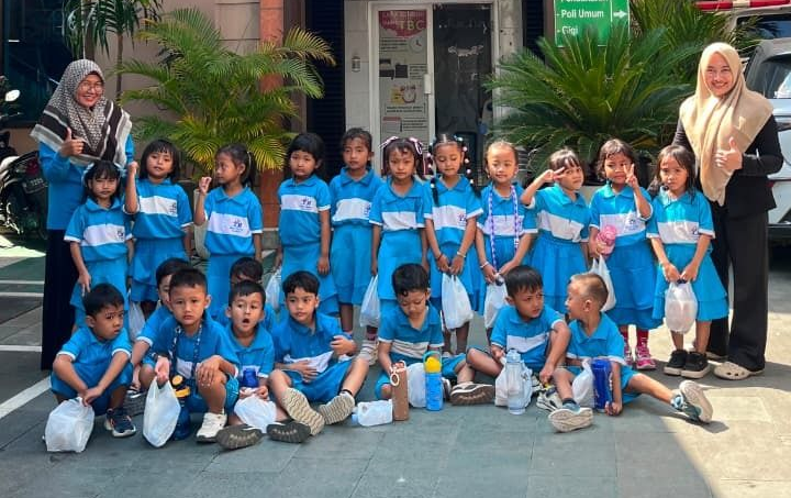 Group of children in blue uniforms posing outside Mutiara Hati building, with adults on either side