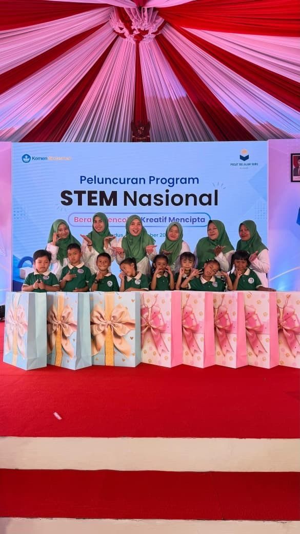 Group on stage under pink drapes at a STEM Nasional event banner, seated behind a decorated table.