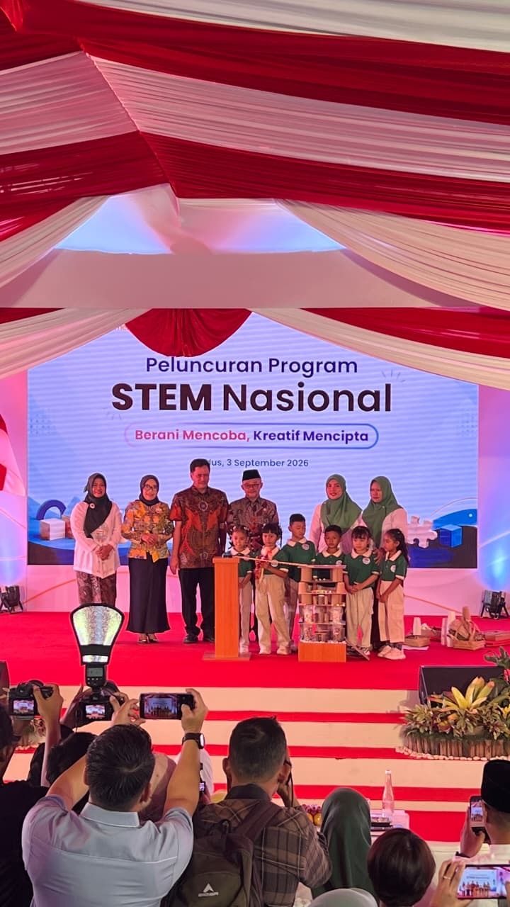 Group of people on a red stage at STEM Nasional event with a large banner and photographers in front