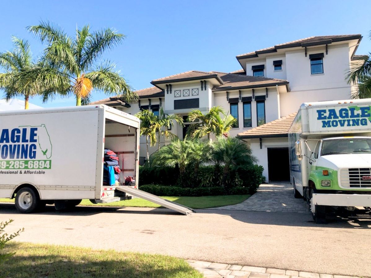 Two moving trucks with a loading ramp parked in the driveway of a two-story home.