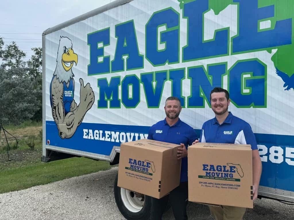 Two Eagle Moving workers holding boxes in front of an Eagle Moving truck trailer.