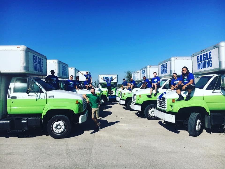 People on green-and-white trucks lined up in an industrial lot under a clear blue sky.