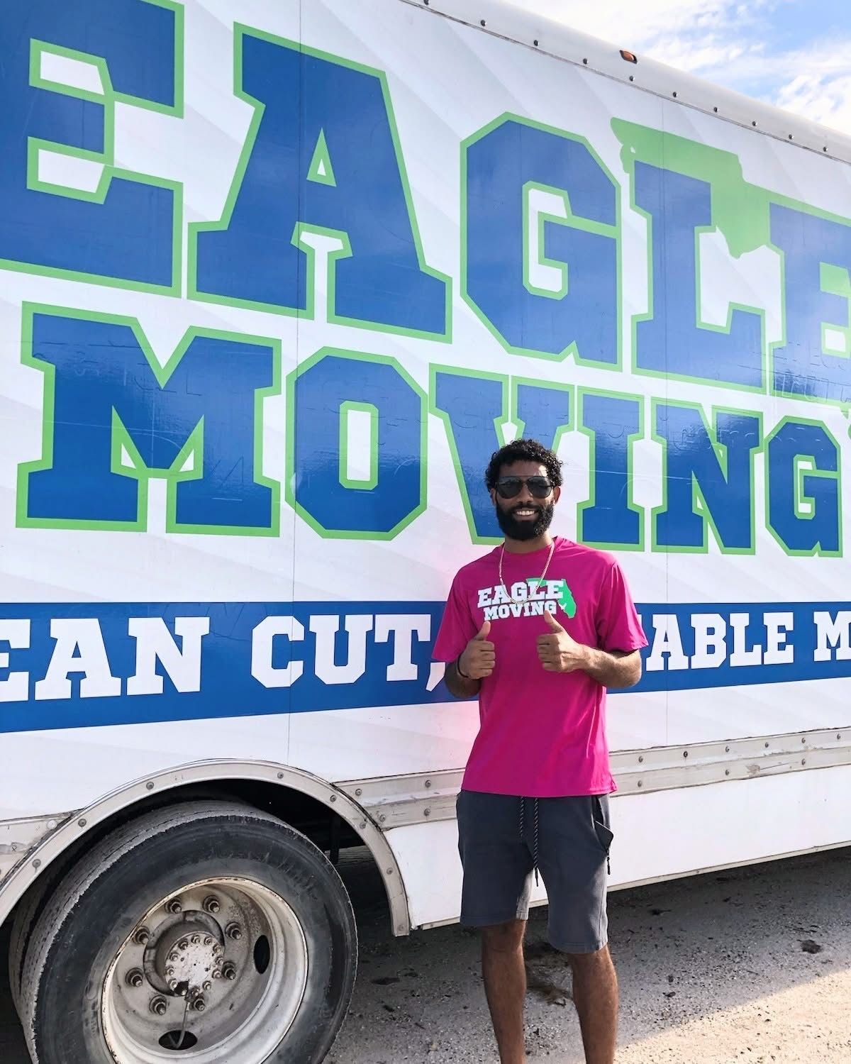 Man standing beside an Eagle Moving truck, holding a drink and wearing a pink shirt.