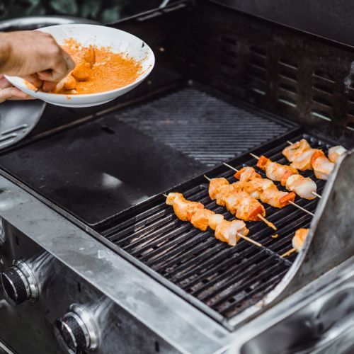 Chicken skewers cooking on a grill while a hand brushes them with orange marinade