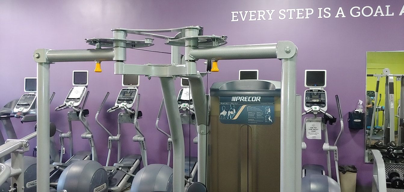 Purple gym with exercise machines and a motivational wall slogan reading “Every step is a goal.”
