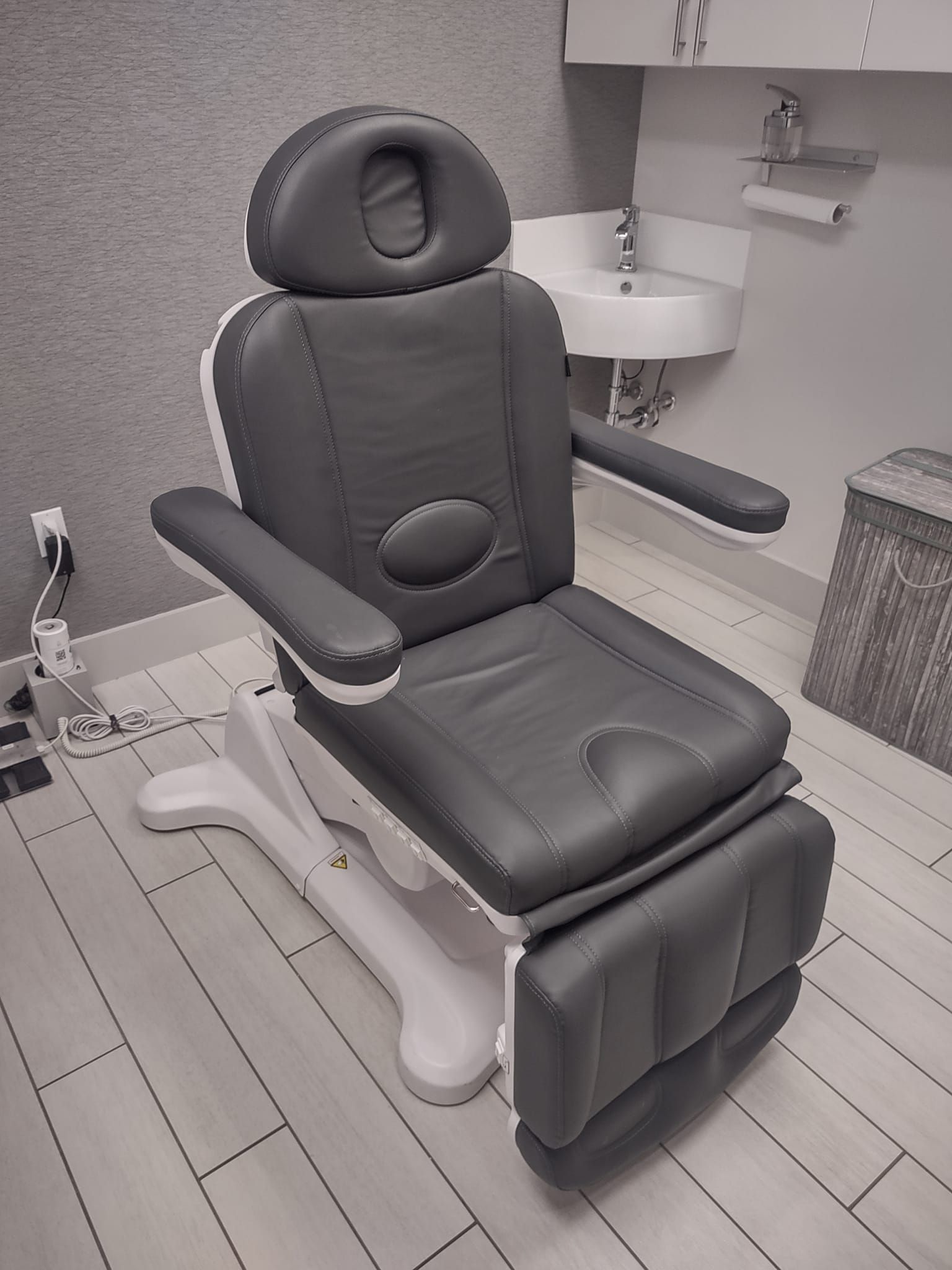 Padded gray treatment chair in a clean medical room with footrest and armrests