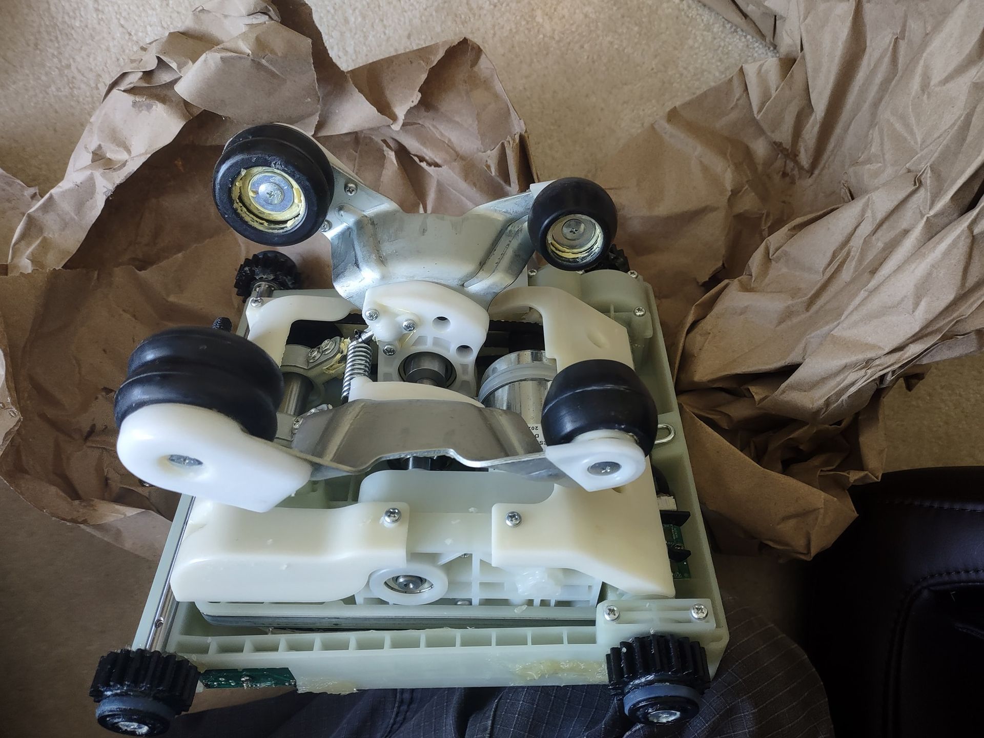 White robot with black wheels and lights lying on crumpled brown paper inside a box