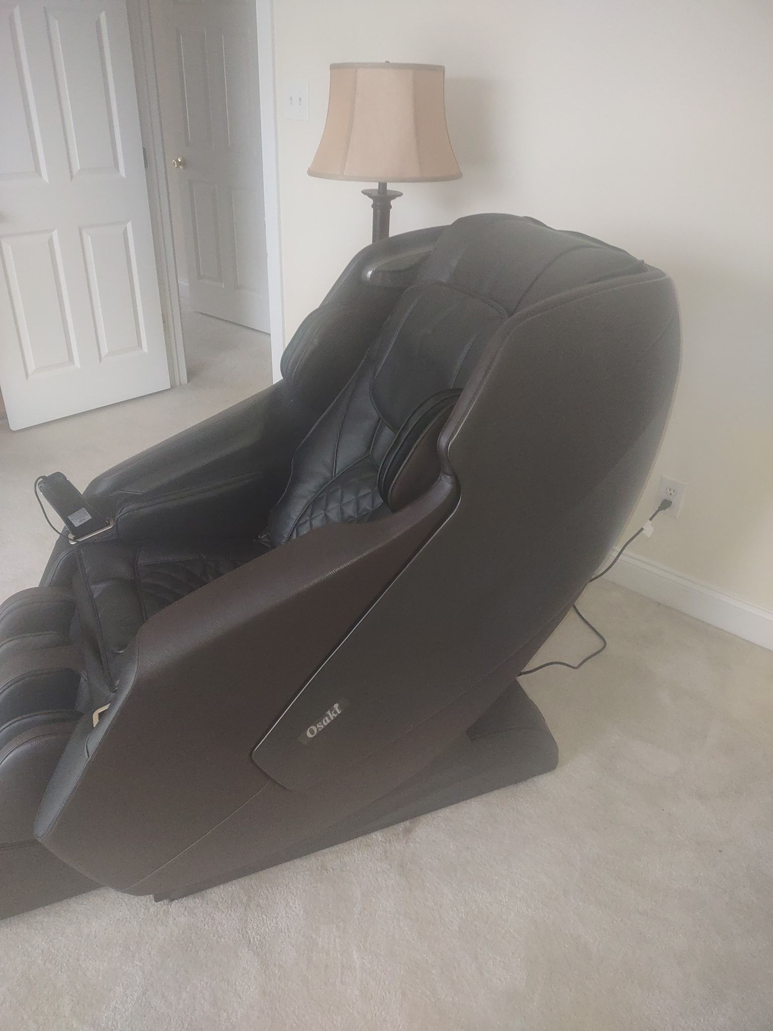 Dark brown recliner chair in a beige room beside a floor lamp and white door.