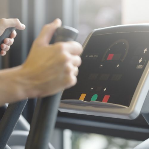 Hands gripping a treadmill console with illuminated buttons in a gym