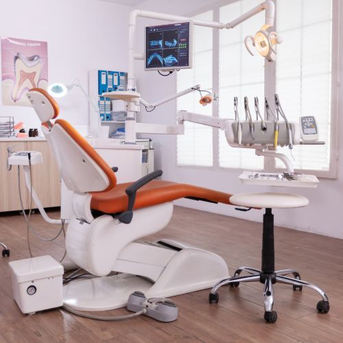 Modern dental exam room with orange chair, overhead monitor, tools, and bright white cabinetry.