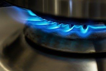 A pot is cooking on a gas stove with blue flames coming out of it.