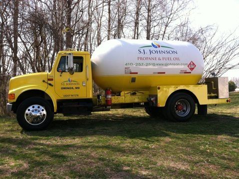 A yellow propane truck is parked in a grassy field