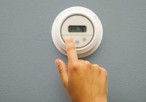 A person is pressing a button on a thermostat.