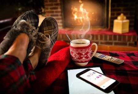 A person is sitting in front of a fireplace with their feet up and a cup of coffee.