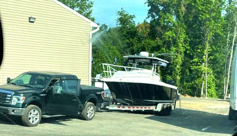 A black truck is towing a boat on a trailer.