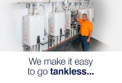 A man in an orange shirt is standing in front of a row of water heaters.