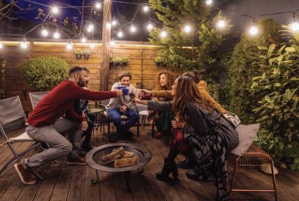 A group of people are sitting around a fire pit on a deck.