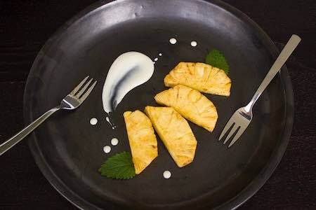 A black plate topped with pineapple slices and a fork.