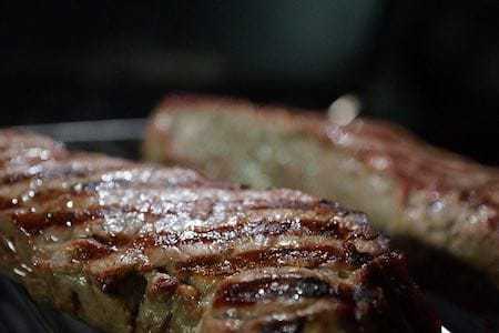 A close up of two steaks cooking on a grill.