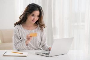 A woman is holding a credit card while using a laptop computer.