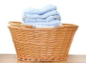A wicker laundry basket filled with clothes on a wooden table.