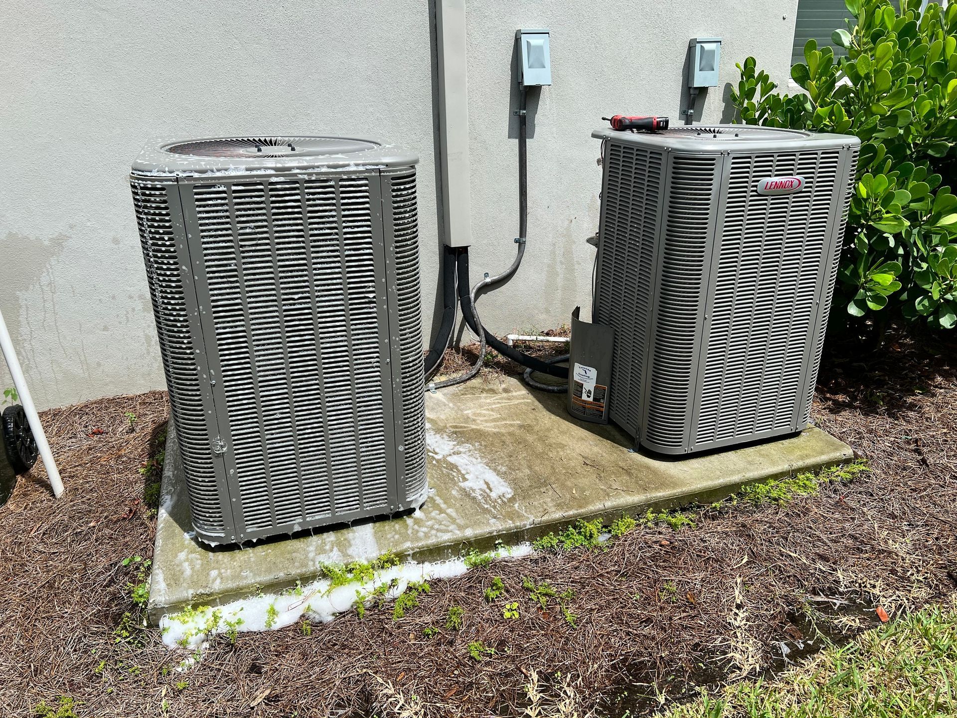 two air conditioners are sitting next to each other on the side of a building .