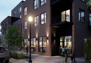 Modern brick apartment building at dusk with lit windows, street trees, and a few people on the sidewalk