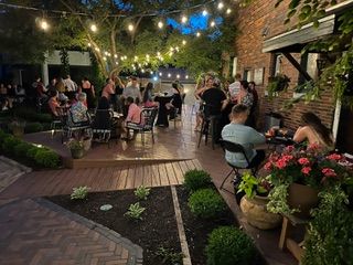String-lit outdoor patio with seated guests, tables, and potted flowers at a brick restaurant
