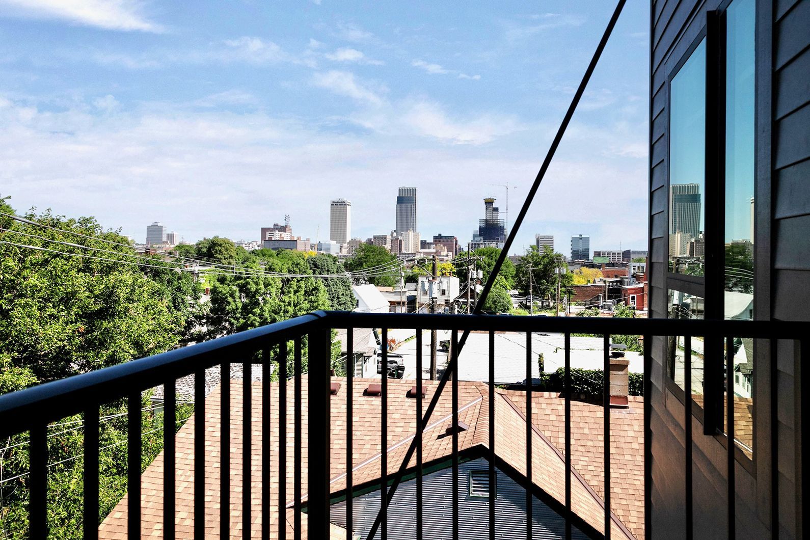 City skyline view from a balcony with black railing, trees, and rooftops under a clear sky